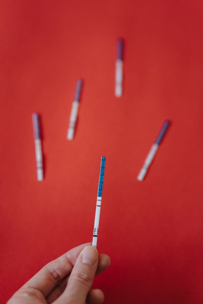 Close-up of a hand holding a pregnancy test strip against a bright red background.